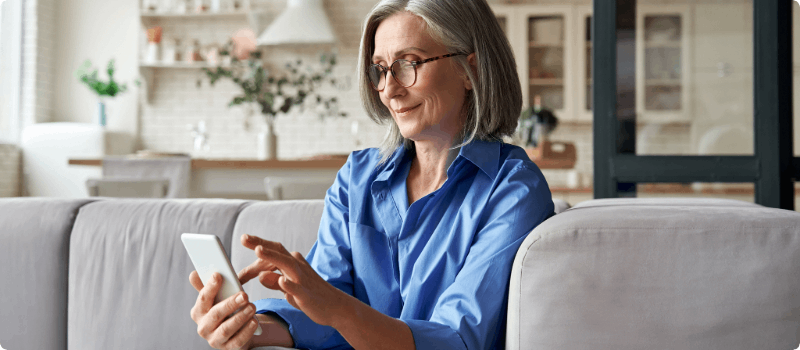 A smiling person sitting on their couch while looking at their phone.