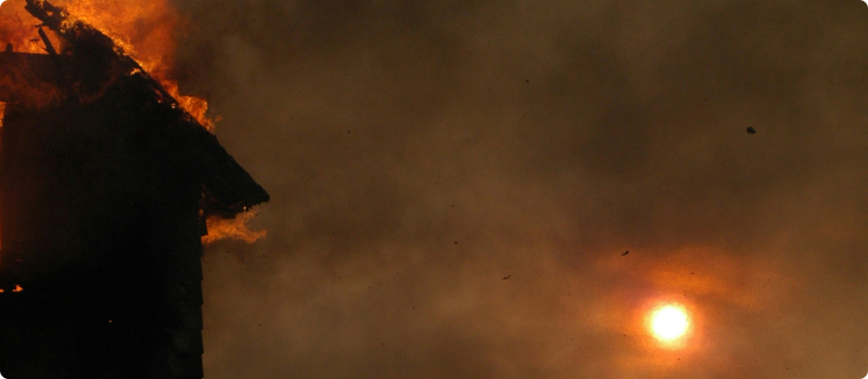 A close-up of an ablaze-house and the surrounding skies filled with black smoke.