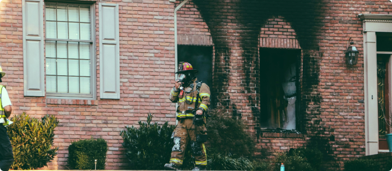 A firefighter walking out of a fire-damaged home.