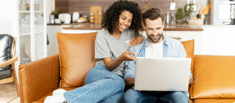 Happy couple sitting on a couch with a laptop.