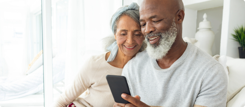 A happy couple sitting together on their couch while looking at their phone.