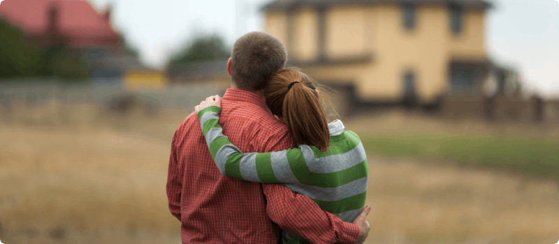 A young couple embracing while standing in front of a home.