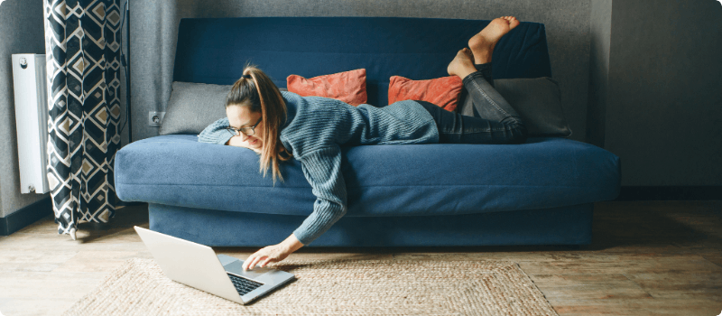 Person lying on a couch while working on her laptop. 