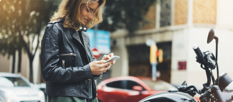 A person standing near their motorcycle, looking at their phone.