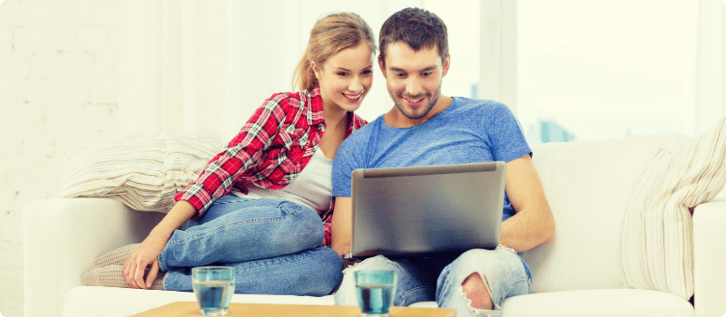 Happy couple sitting on a couch while looking at a laptop.