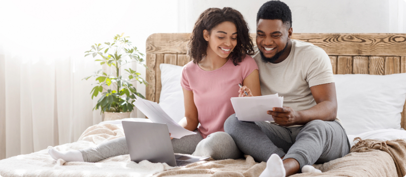 A happy couple reviewing documents together while sitting together on their bed.