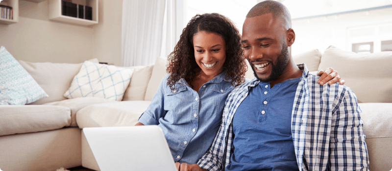 Happy couple sitting on their living room floor looking at a laptop. 
