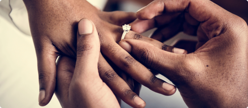 A person placing a diamond ring on their partner's finger.