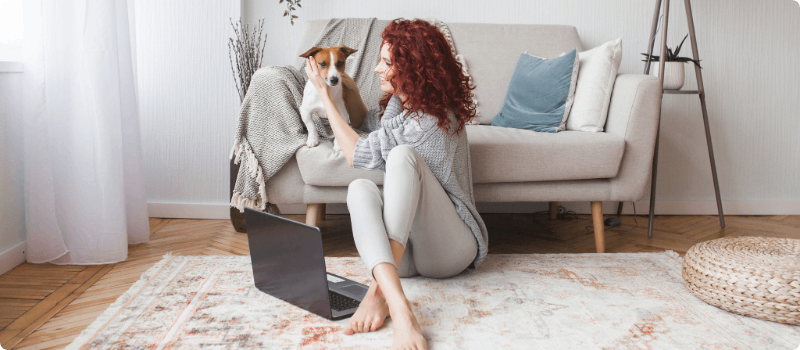 Happy woman, sitting on the floor with her laptop while petting her dog.