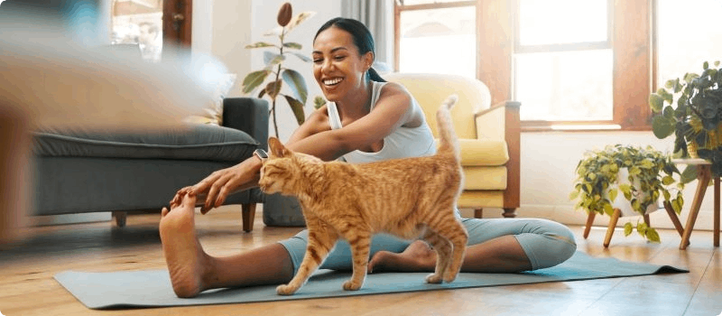 Happy woman stretching on her living room floor with her cat. 