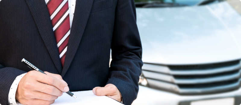 A close-up of an insurance agent standing in front of a car with a clipboard.