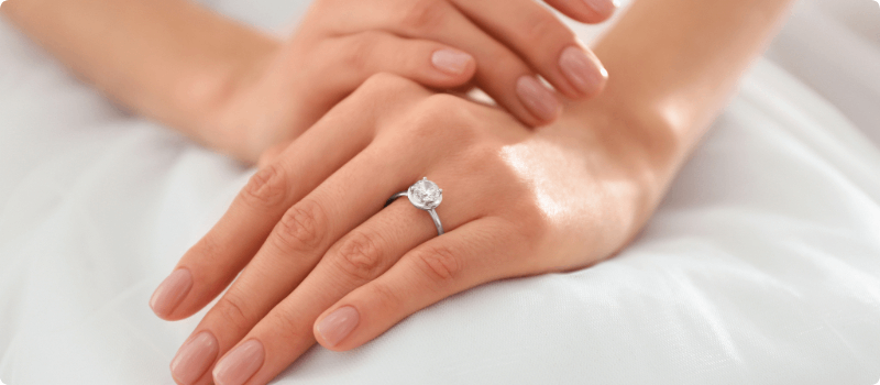 A bride with her hands folded on her lap, showcasing her new diamond ring.