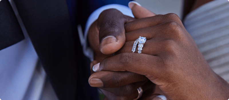 A bride and groom holding hands, showcasing a diamond wedding ring.