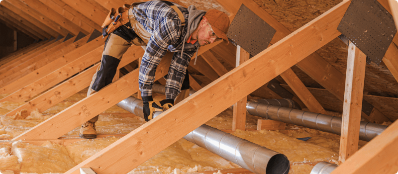 A construction worker adding ventilation ducts to an attic.