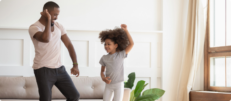 A father dancing with his daughter in their living room.