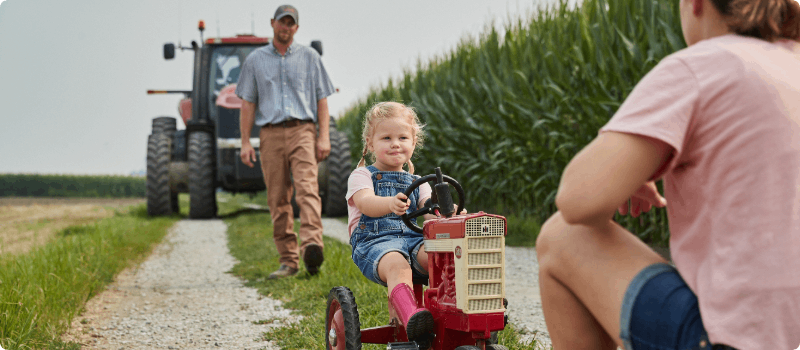 A small family on a road with a tractor in the background.