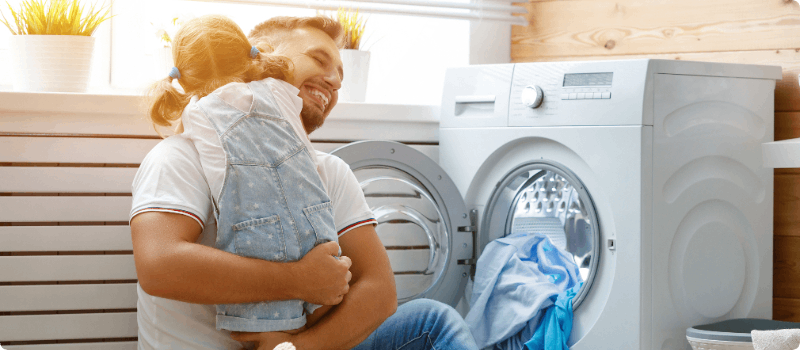 A parent embracing his daughter while doing laundry.