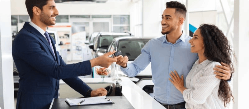 Couple buying a new car from a salesperson at a dealership. 