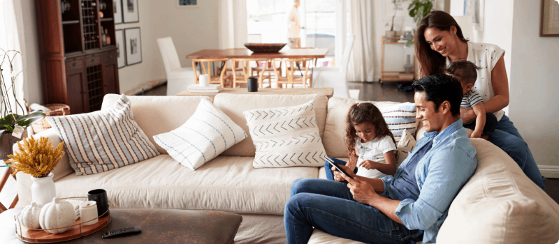 A family sitting on their living room couch together while looking at a computer tablet.