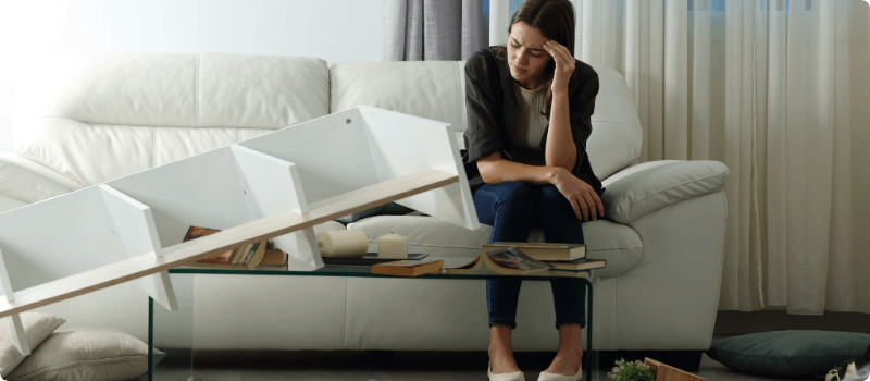 Worried person sitting on the couch in a damaged living room.  