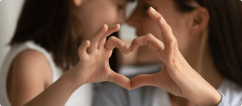 A close-up of a parent and child joining hands to make the shape of a heart.