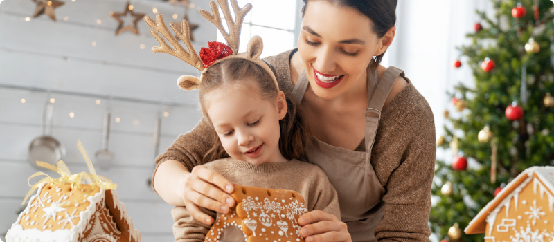 A parent making a gingerbread house with their child.