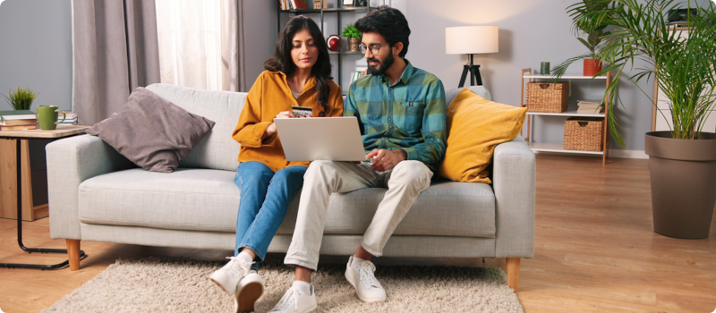 a man and woman sitting on a couch looking at a laptop