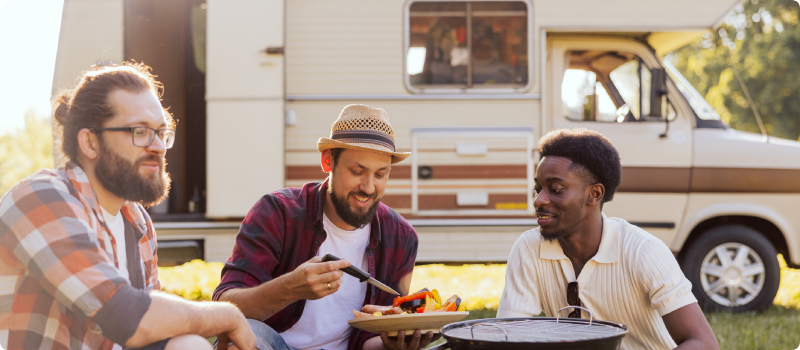 a group of three men cooking outside an RV