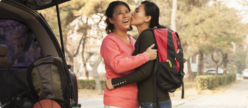 Mother and daughter embracing behind car on college campus