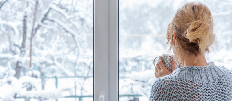 A woman looks out of the window at the snow-covered outdoors.
