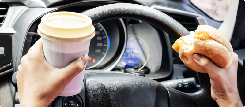 a person driving while holding coffee and food