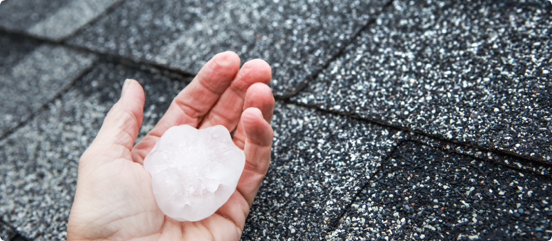 a person holding a piece of hail against a roof