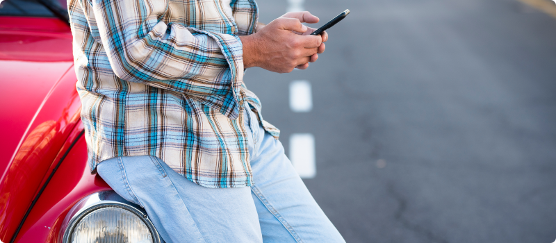 a man looking at his phone while leaning against a car