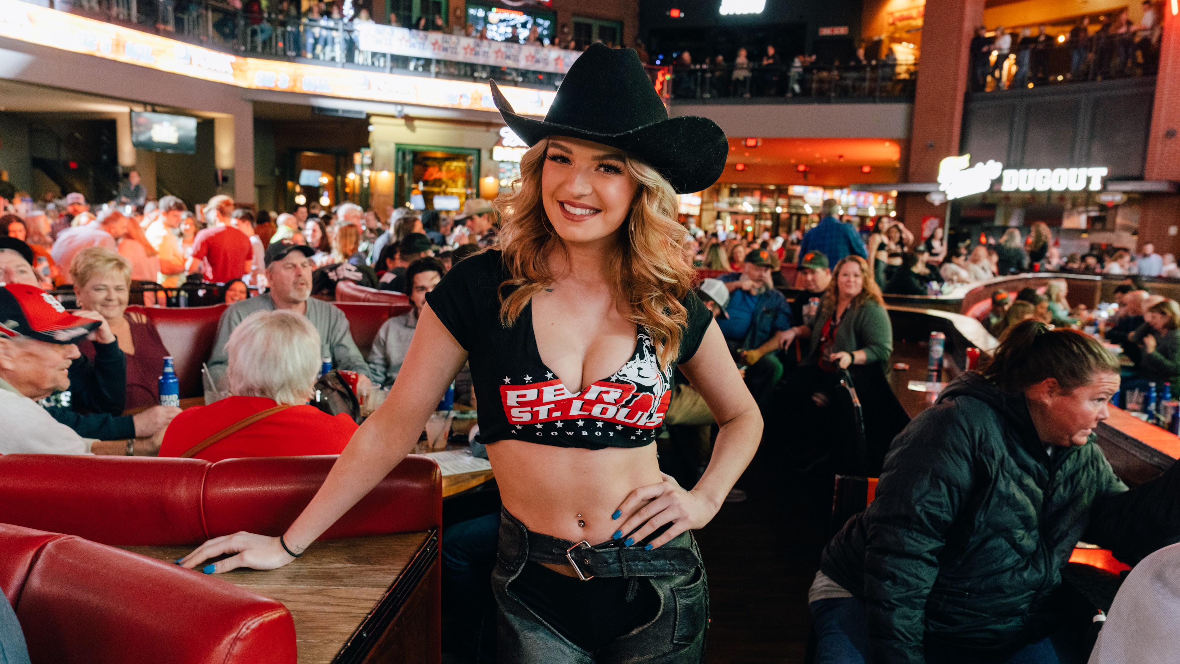 PBR Buckle Bunny in cowboy hat surrounded by guests at Ballpark Village venue.