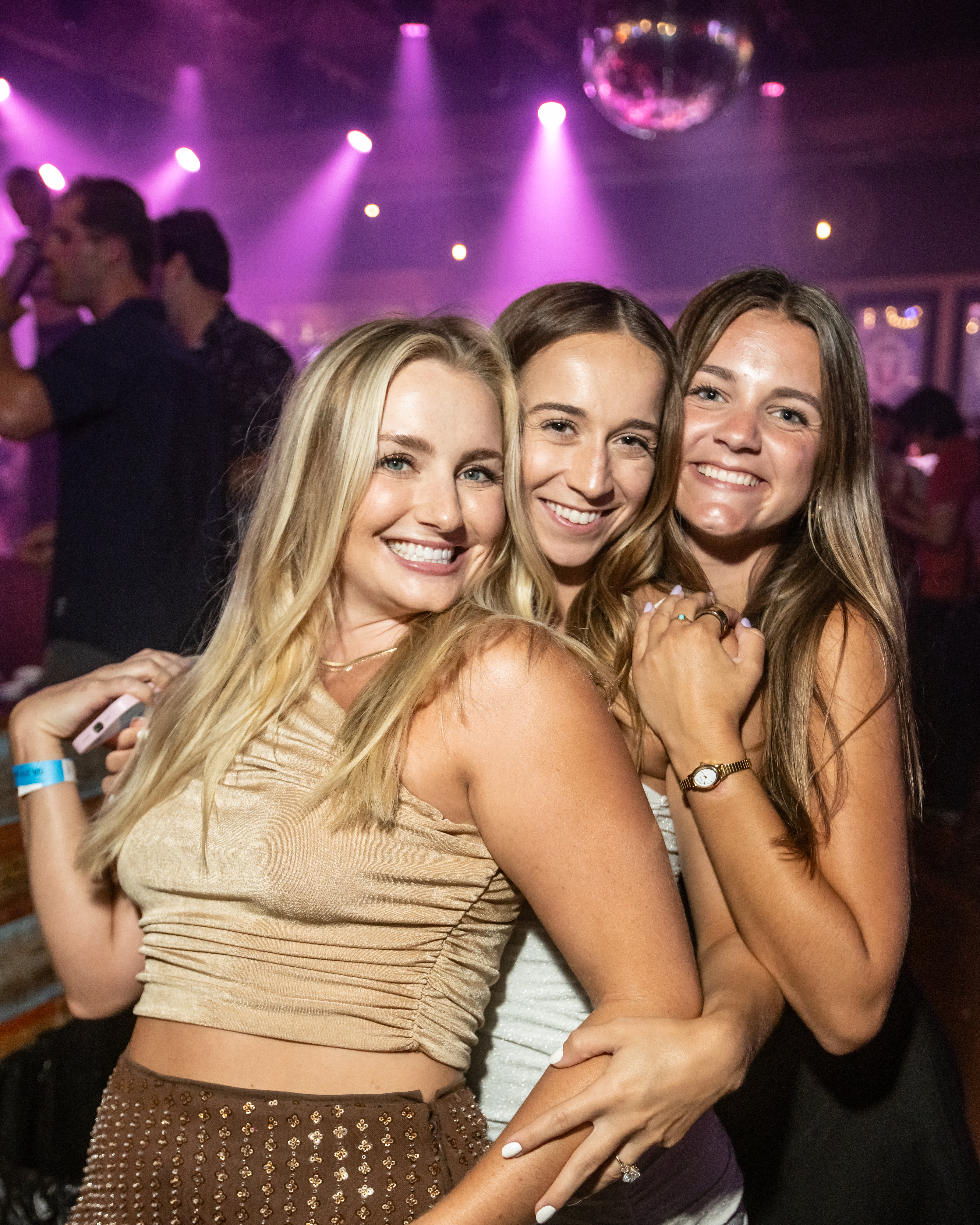 Three ladies at PBR Big Sky, pink club lights and disco ball in background