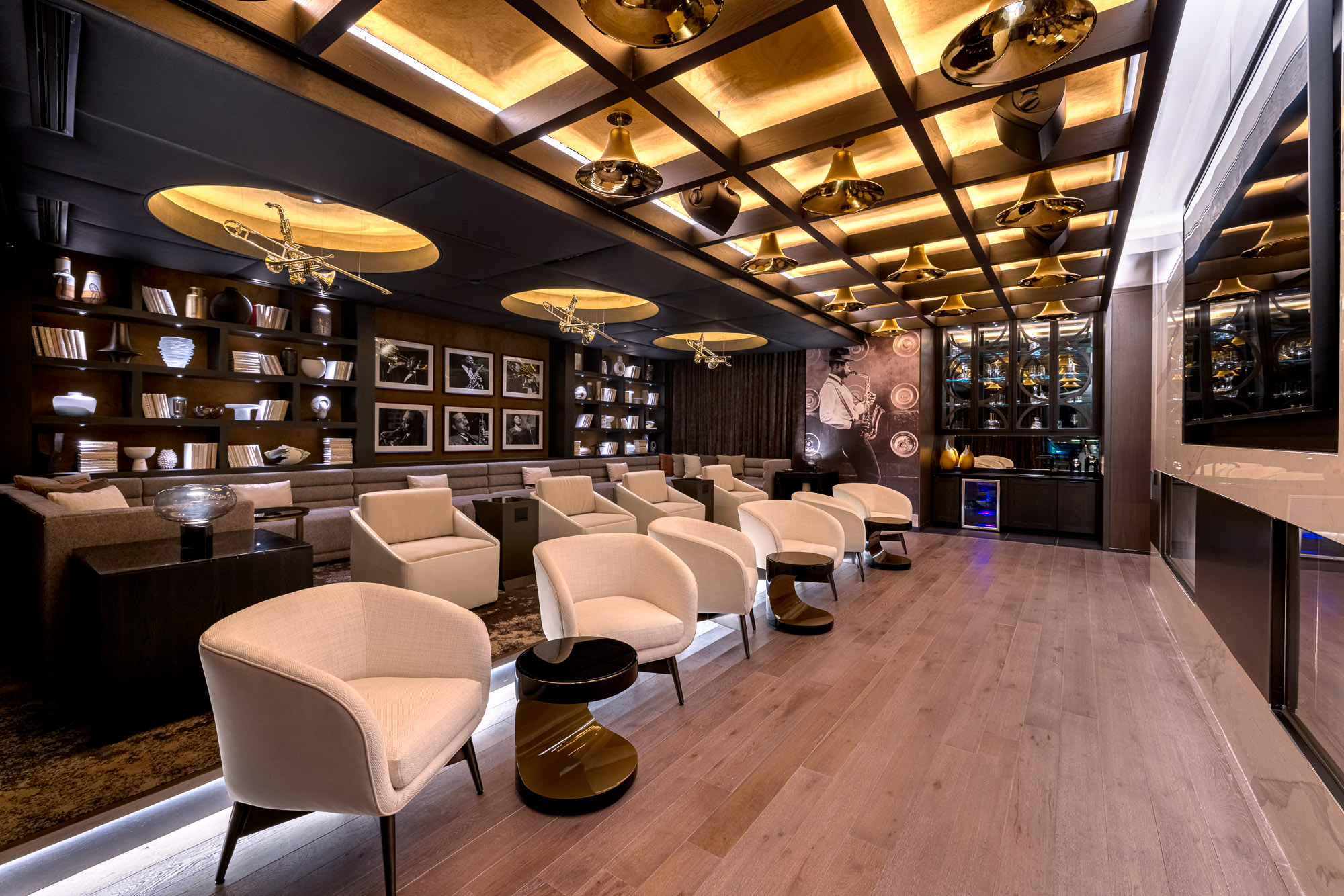 Large screen TV on wall and viewing area with chairs and couches at Three Light luxury apartment building.