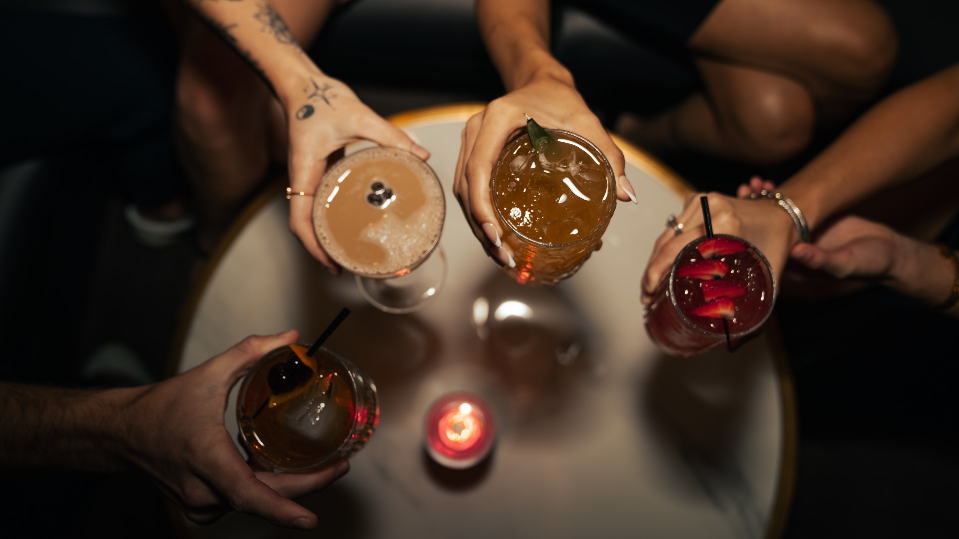 Overhead photo of cocktails being toasted by group of friends at Houndsmen Lounge at Live! at the Pointe Orlando.