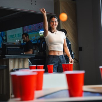 Woman in a white crop t-shirt and black pants playing table pong at Sports & Social at Live! at the Pointe Orlando.