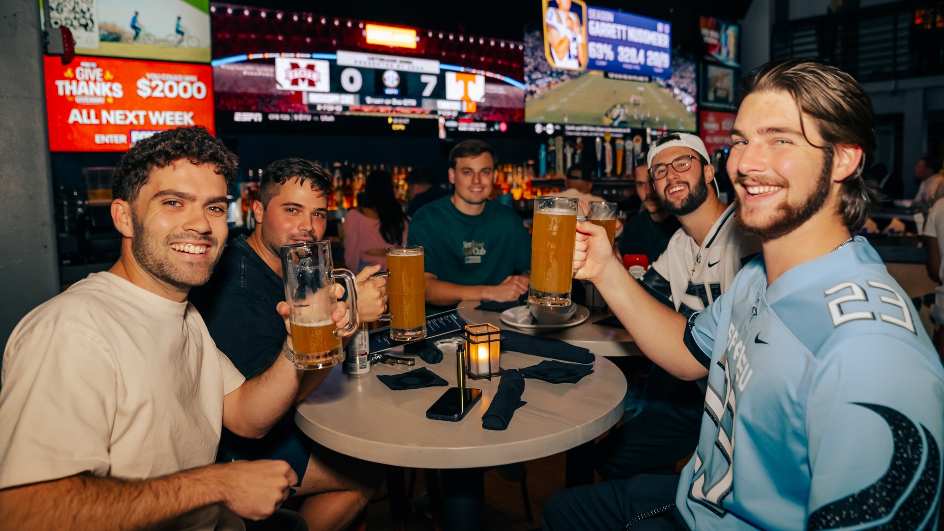 Group of male friends enjoying drinks (beer) and watching sports on the big screen TVs at Sports & Social at Live! at the Pointe Orlando.