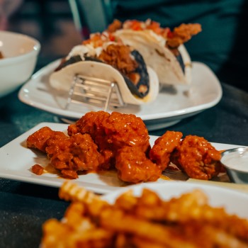 Crinkle french fries, saucy chicken wings and ranch, and crispy ancho-spiced chicken soft and crunchy taco on white plates wrap at Sports & Social at Live! at the Pointe Orlando.