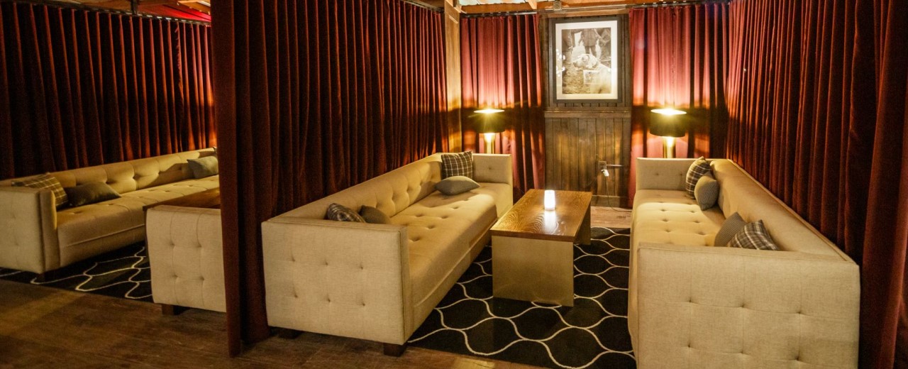 Private seating areas with sofas and tables, separated by velvet curtains at Houndsmen Lounge at Live! at the Pointe Orlando.