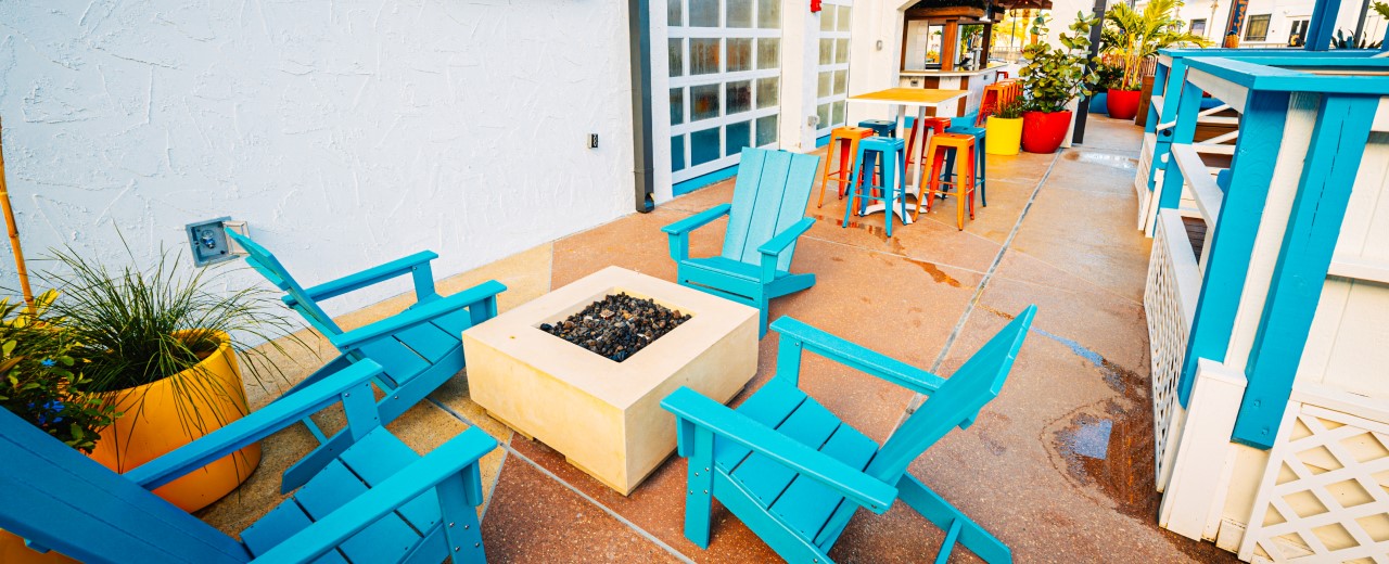 Outdoor patio with fire pit, teal adirondack, and bar at Shark Bar at Live! at the Pointe Orlando.
