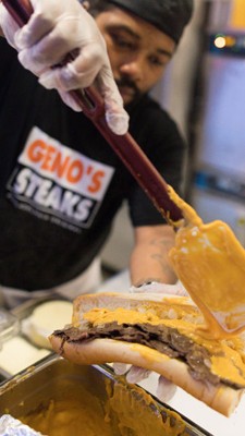Geno's Steaks employee putting cheese on steak hoagie.