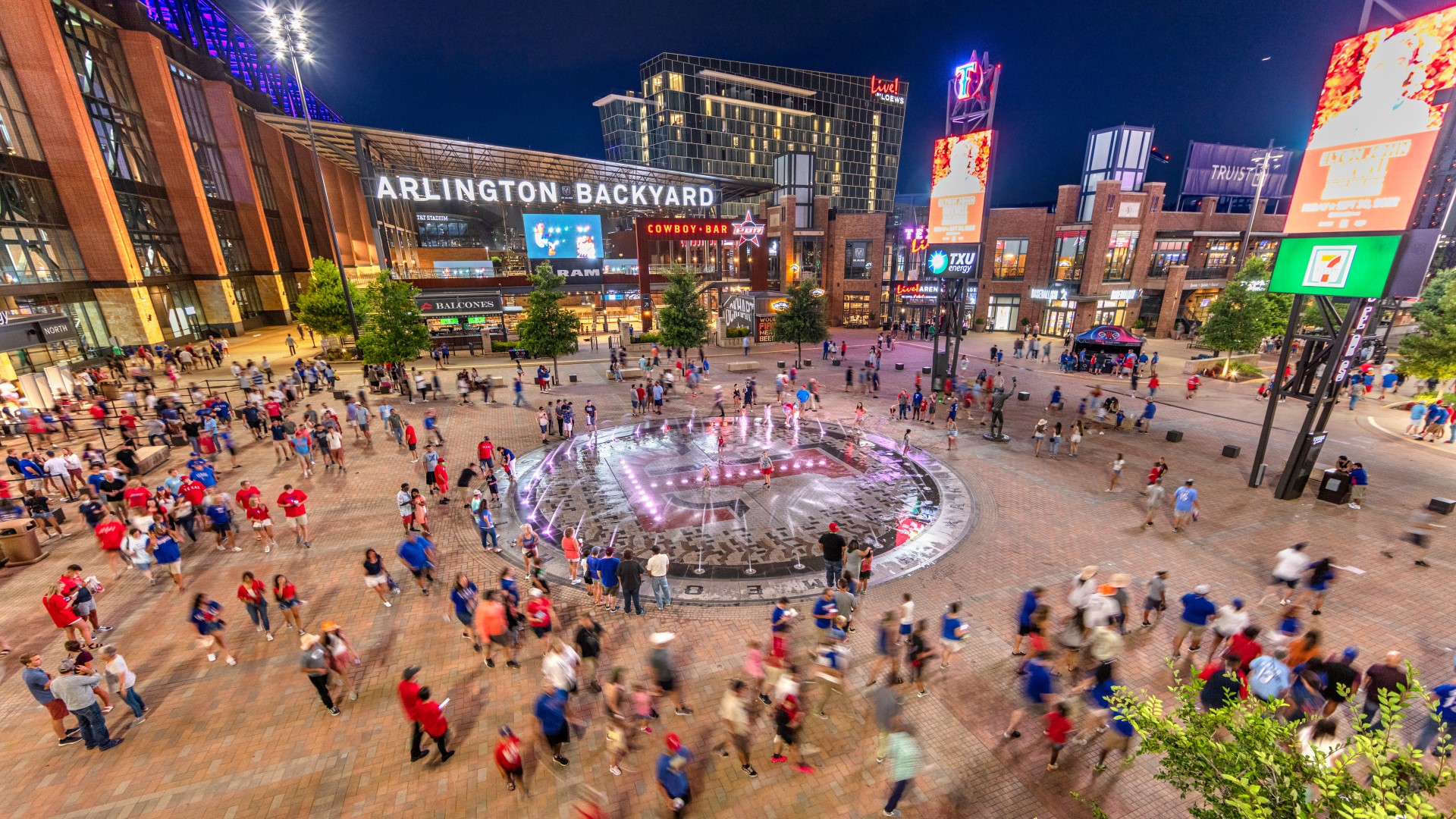 Groups of people walking around Arlington Backyard outdoor space at night at Texas Live!