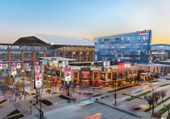 Outside of beautiful Texas Live!, featuring a tall mirrored Live! by Loews hotel that reflects structures and skies.