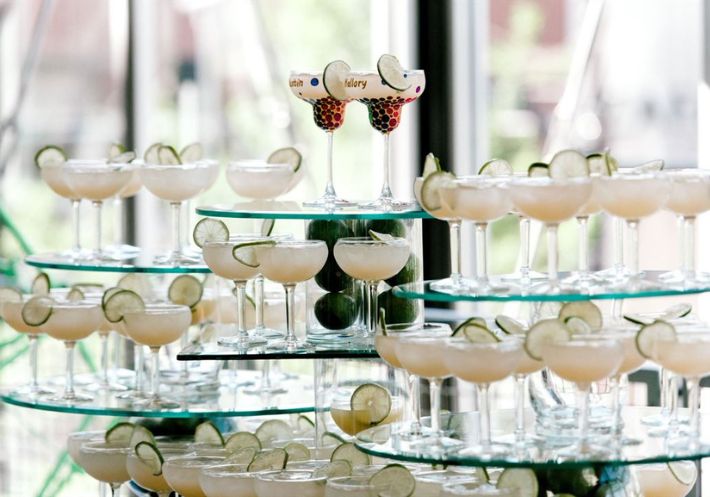 A wedding cocktail tower featuring lime-garnished glasses is topped off by two marked just for the happy couple!