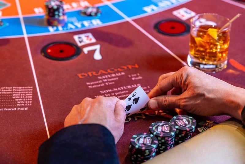image of a Baccarat table with a hand showing some chips and a playing card