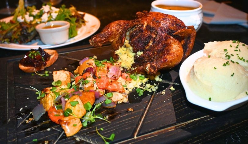 image of a plate of mixed greens salad, a wooden board with a small roasted cornish hen with stuffing, a bowl of two scoops of mashed potatoes, and a small bowl of butternut squash soup. this feature is the prime rib's thanksgiving menu at live! louisiana