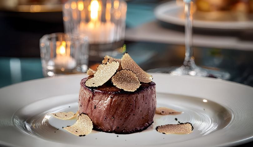image of a small steak and shaved truffle on top next to a glass of wine
