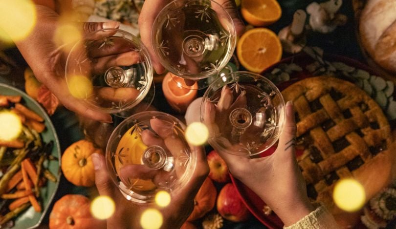 image of a table of thanksgiving food and people clinking cocktail glasses together in the center